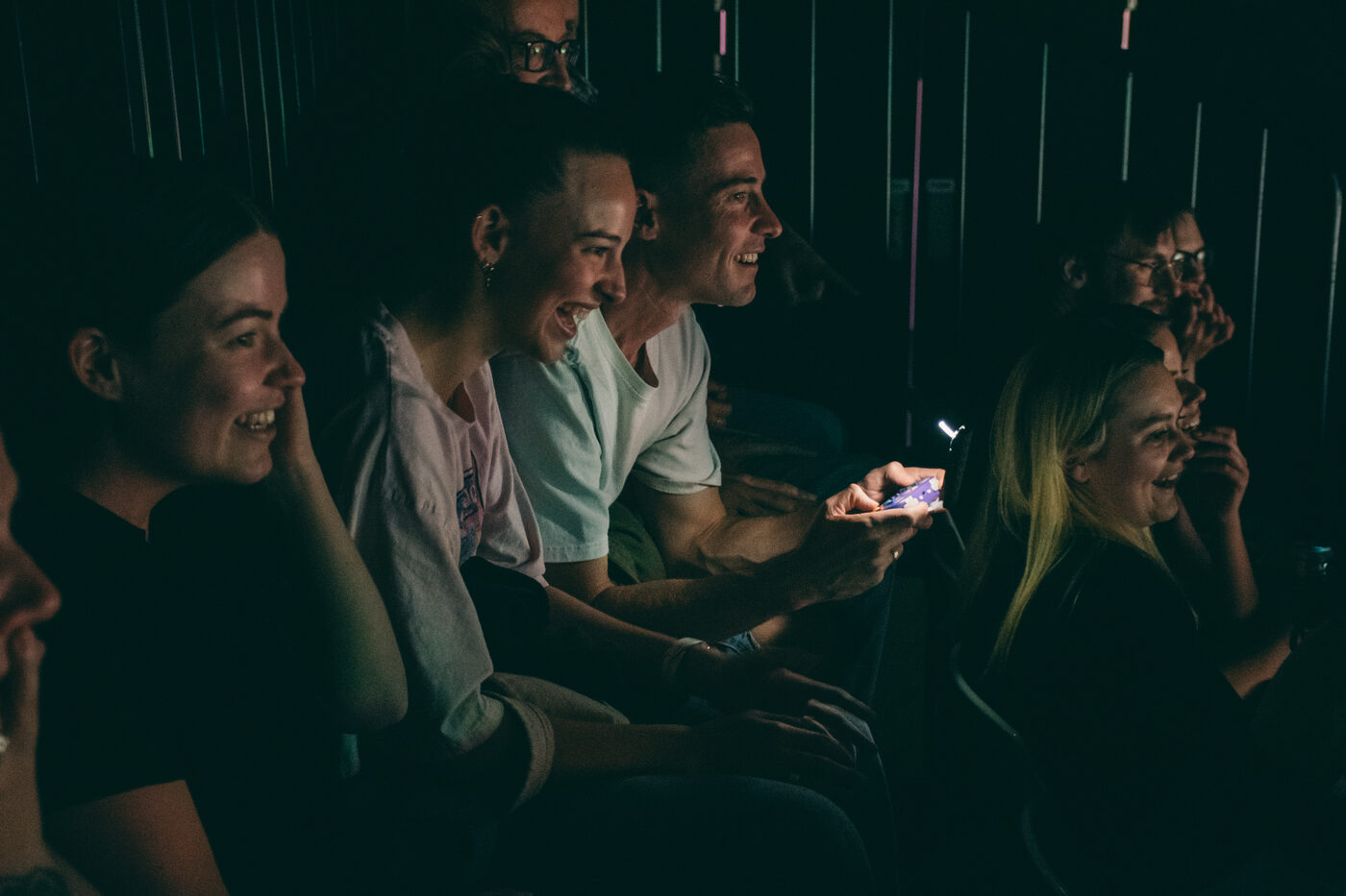 Laughing audience members passing a video game controller during a live performance of Karate Man